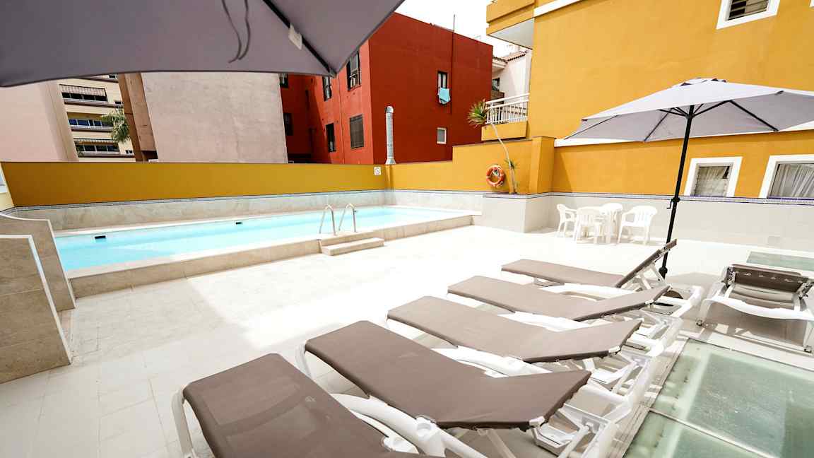 Udendørs pool med liggestole og parasoller på et stenbelagt område. (AI-genereret tekst)