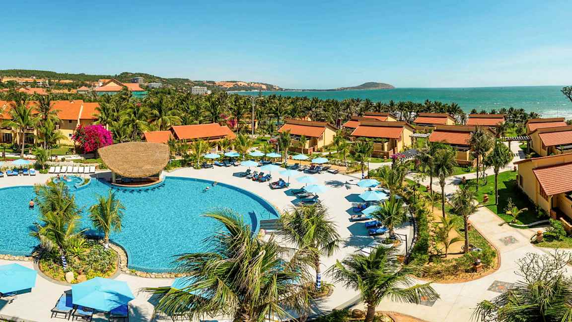 Ferieanlæg med store bygninger med tegltag, palmer og en pool i midten. (AI-genereret tekst)