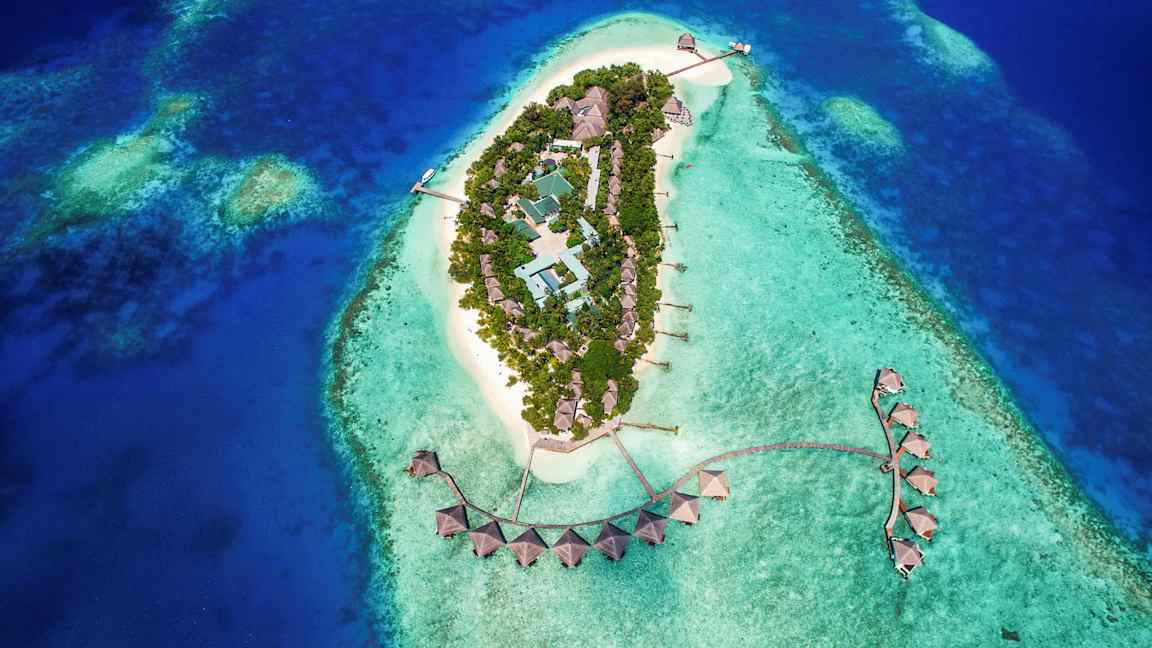 Luftfoto af en tropisk ø med bygninger omgivet af turkisblåt vand. (AI-genereret tekst)