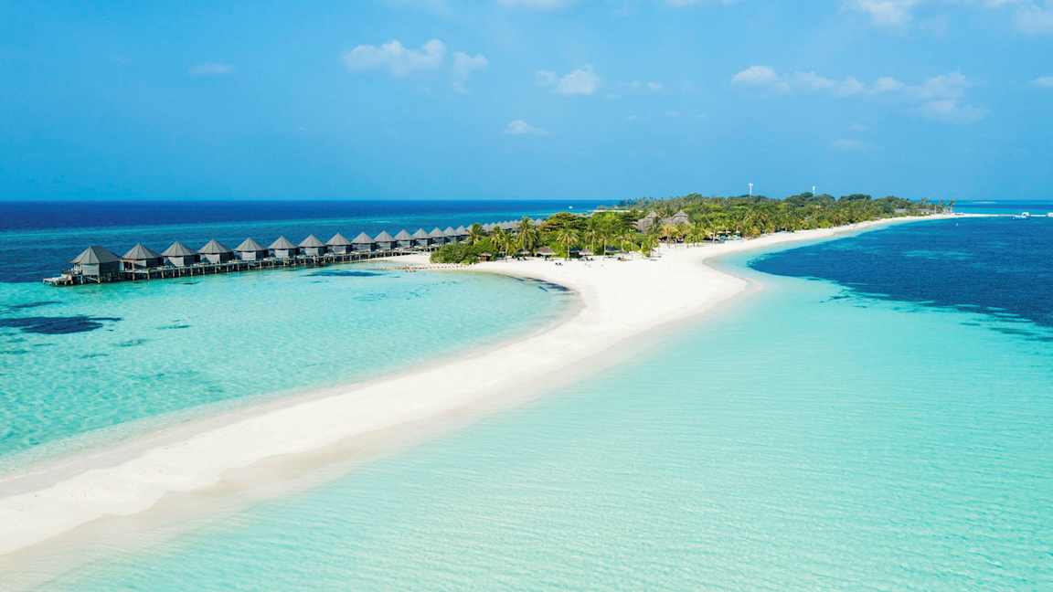En tropisk strand med klart blåt vand, sand og palmer samt vandbungalower på stolper. (AI-genereret tekst)