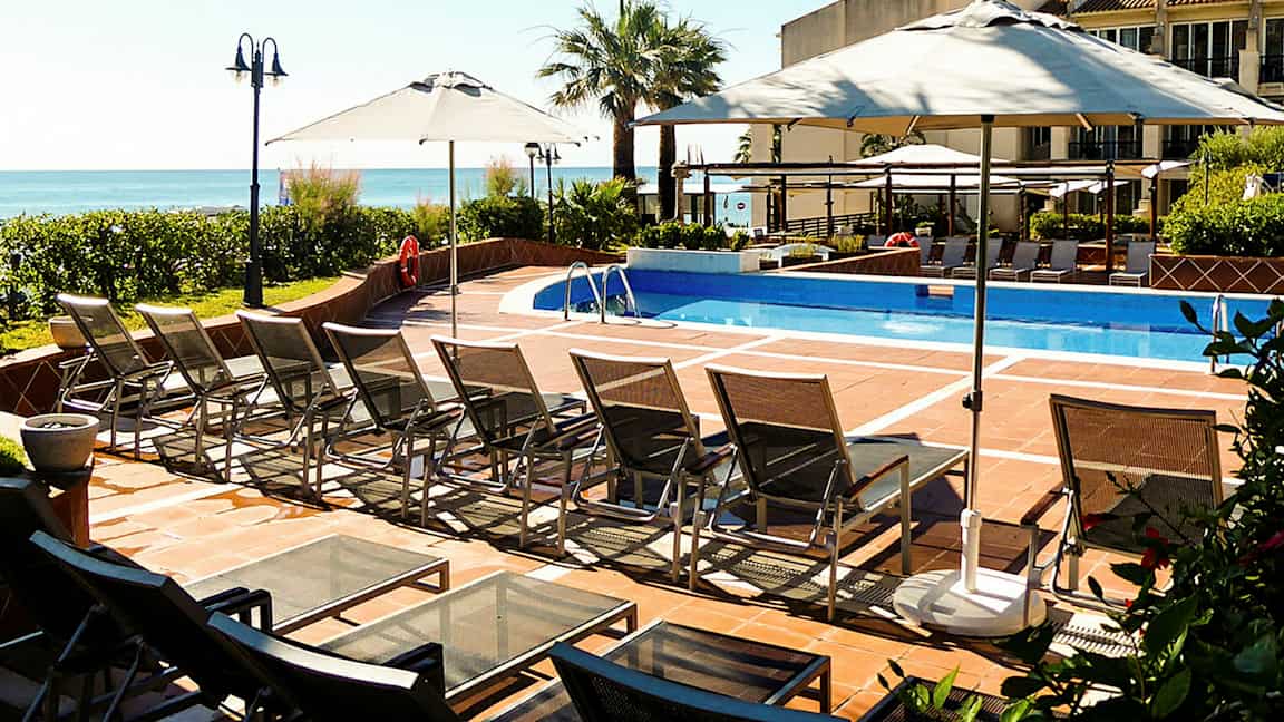 En udendørs pool med liggestole og parasoller. (AI-genereret tekst)