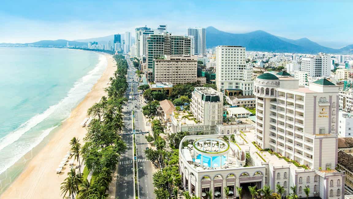 Billede af en by ved havet med moderne bygninger og en strand med parasoller. (AI-genereret tekst)