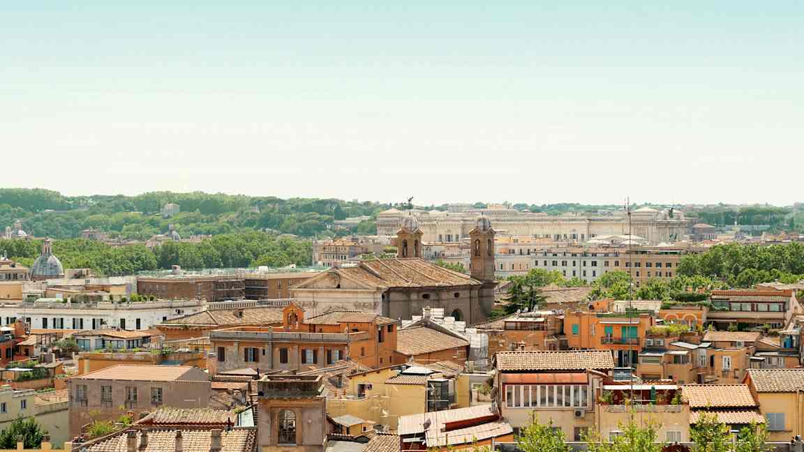 Udsigt over en by med mange bygninger, to kirketårne og grøn vegetation i baggrunden. (AI-genereret tekst)
