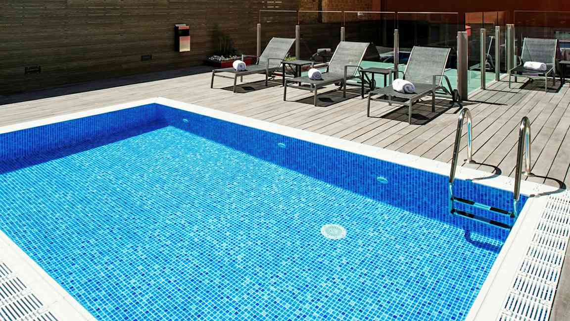 En blå mosaikpool med tilhørende liggestole på en trægulvoverflade. (AI-genereret tekst)