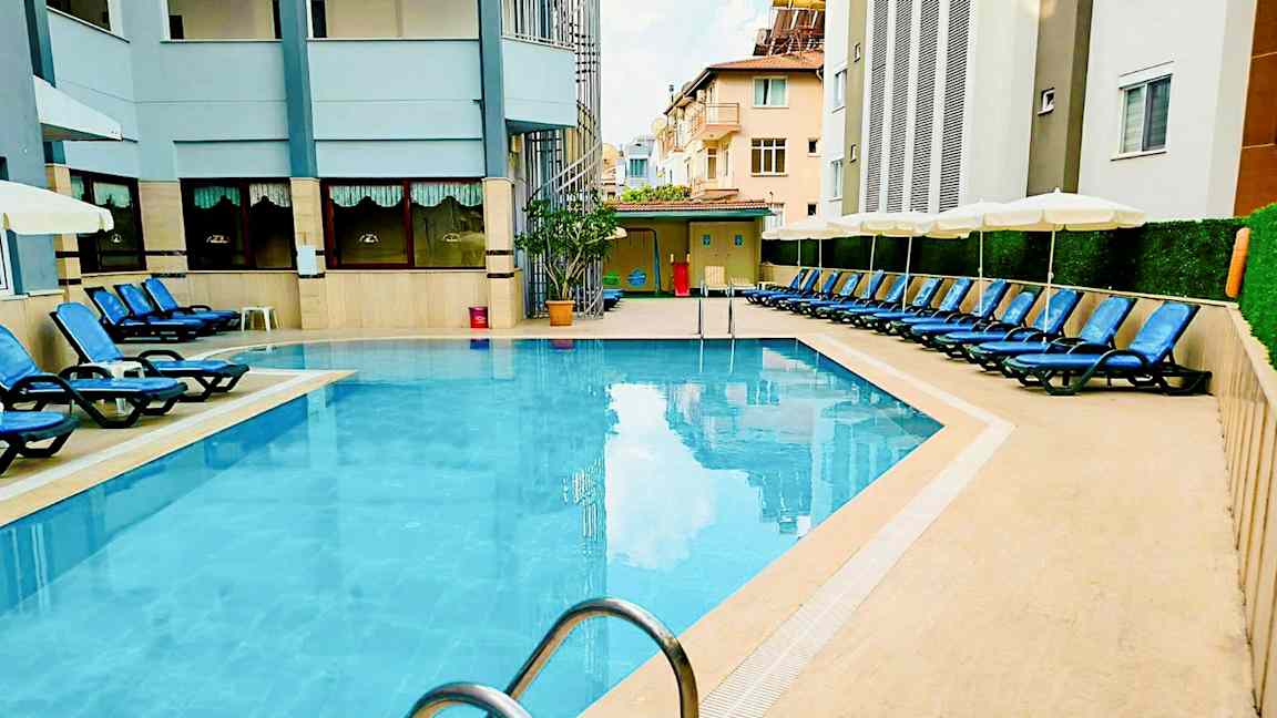 En udendørs pool omgivet af liggestole og bygninger. (AI-genereret tekst)