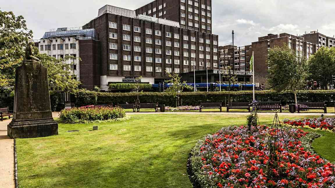 En park med blomster og græsplæne foran en bygning. (AI-genereret tekst)