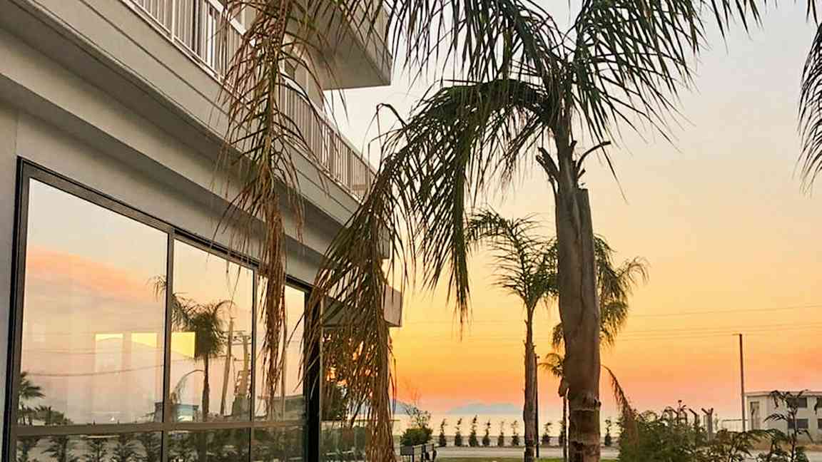 En bygning med glasvinduer og palmer i forgrunden ved solnedgang. (AI-genereret tekst)