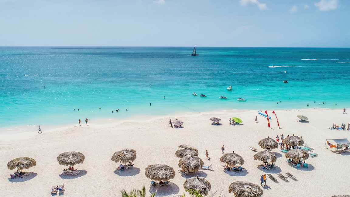 En sandstrand med parasoller og mennesker, der soler og bader i en blå havudsigt. (AI-genereret tekst)