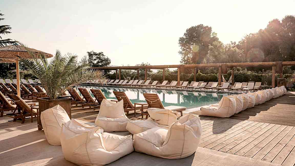 En udendørs pool omgivet af solsenge og sækkestole. (AI-genereret tekst)