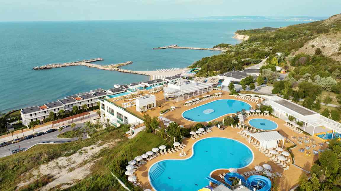 Billede af en ferieresort ved havet med pools, liggestole og frodige omgivelser. (AI-genereret tekst)
