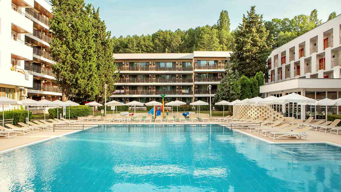 Udendørs swimmingpool med liggestole og parasoller, omgivet af moderne bygninger og grønt. (AI-genereret tekst)