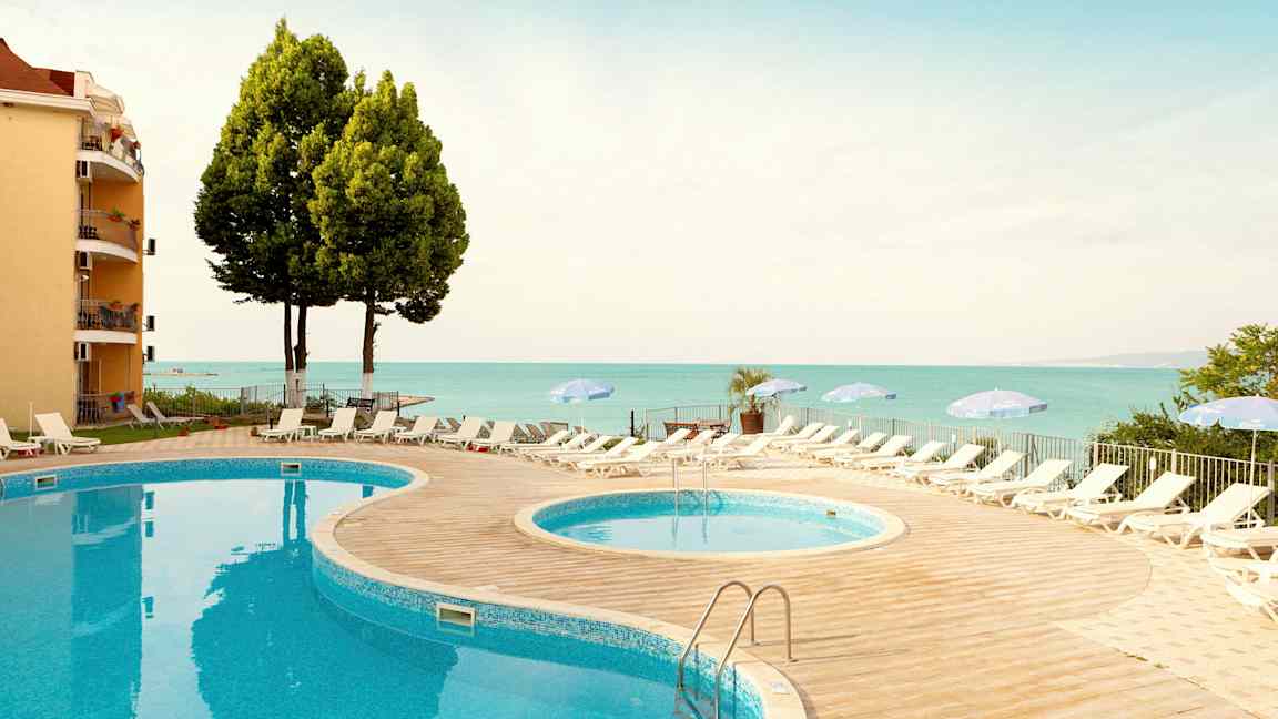 To pools med solsenge og paraplyer på et sted nær havet. (AI-genereret tekst)