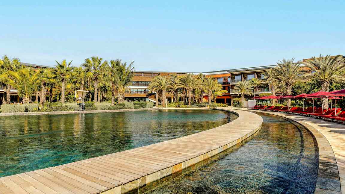 En pool med en træbro omgivet af palmer ved et hotel. (AI-genereret tekst)