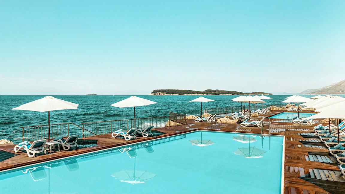 En swimmingpool ved havet, omgivet af solsenge og parasoller. (AI-genereret tekst)