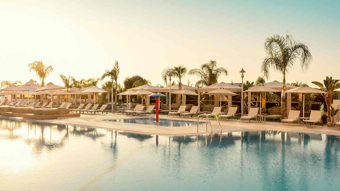 Udendørs pool omgivet af liggestole og parasoller. (AI-genereret tekst)