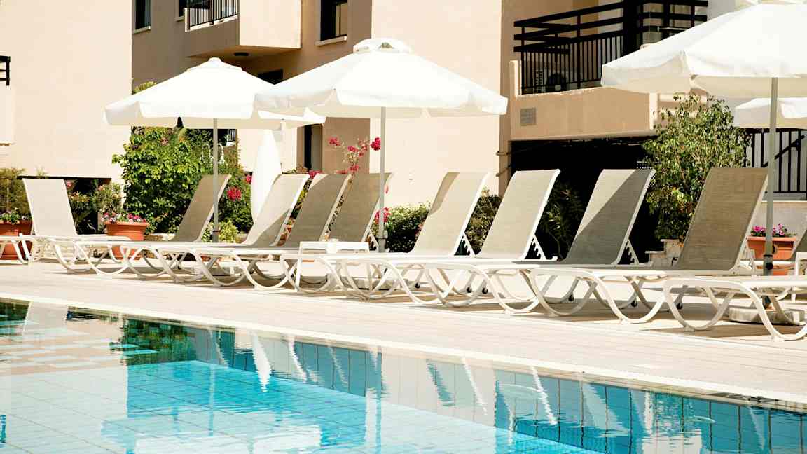 Liggestole ved en pool med parasoller. (AI-genereret tekst)