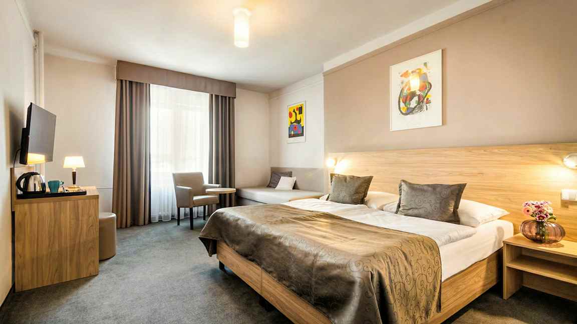 Et hotelværelse med en stor dobbeltseng, et bord med to stole og et vægmonteret TV. (AI-genereret tekst)