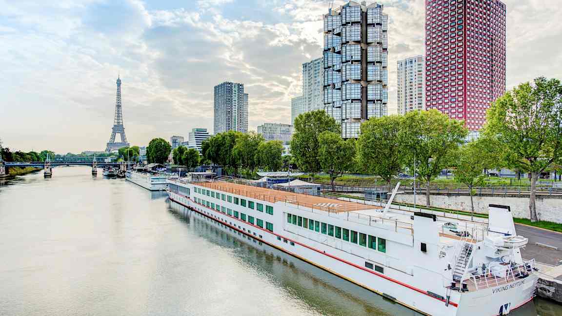 Flod med en båd ved kaj, moderne bygninger og Eiffeltårnet i baggrunden. (AI-genereret tekst)