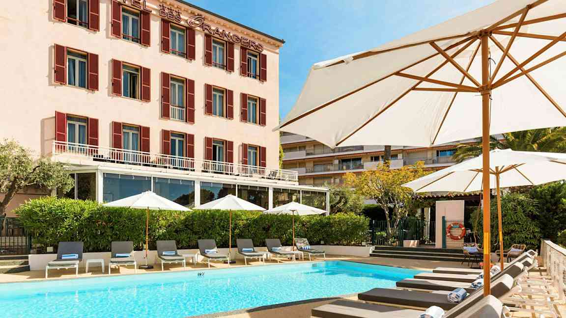 Hotelbygning med pool og liggestole foran. (AI-genereret tekst)