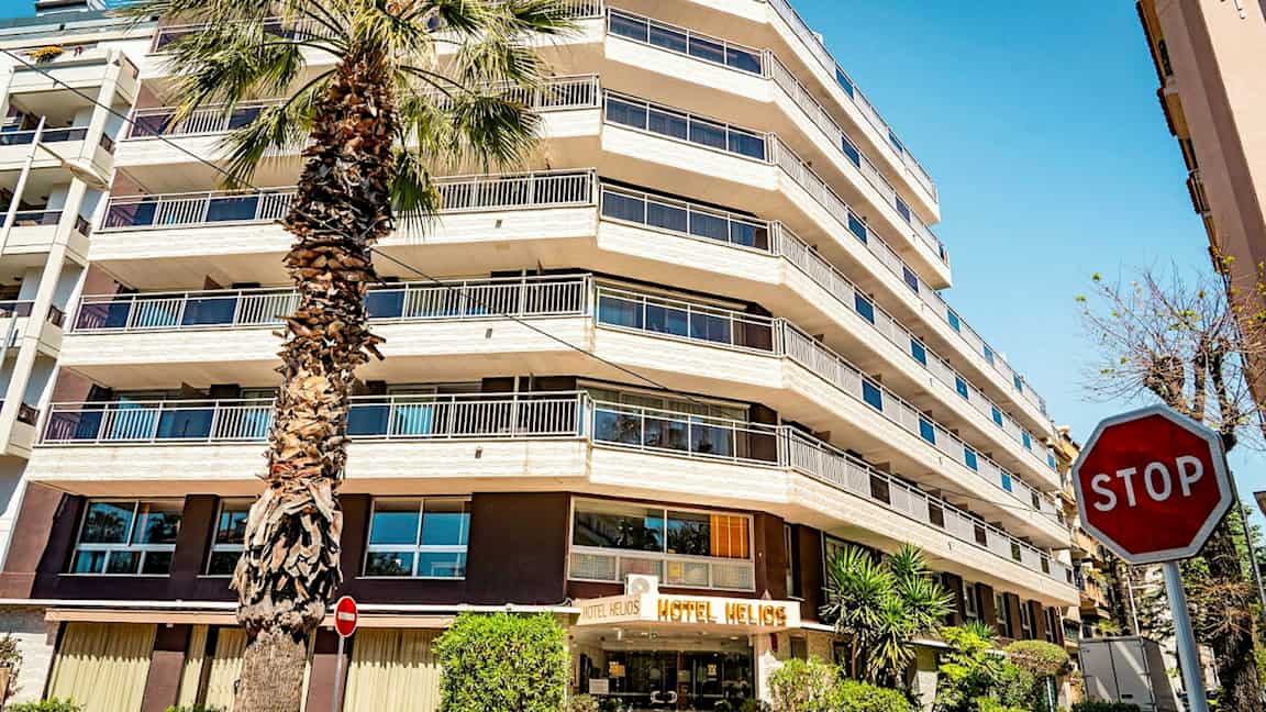 Et hotel med flere etager og et palmetræ foran. Skiltet "STOP" er synligt til højre. (AI-genereret tekst)