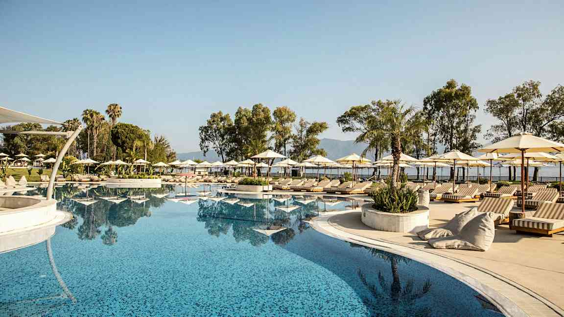 En stor pool omgivet af liggestole, parasoller og palmer. (AI-genereret tekst)