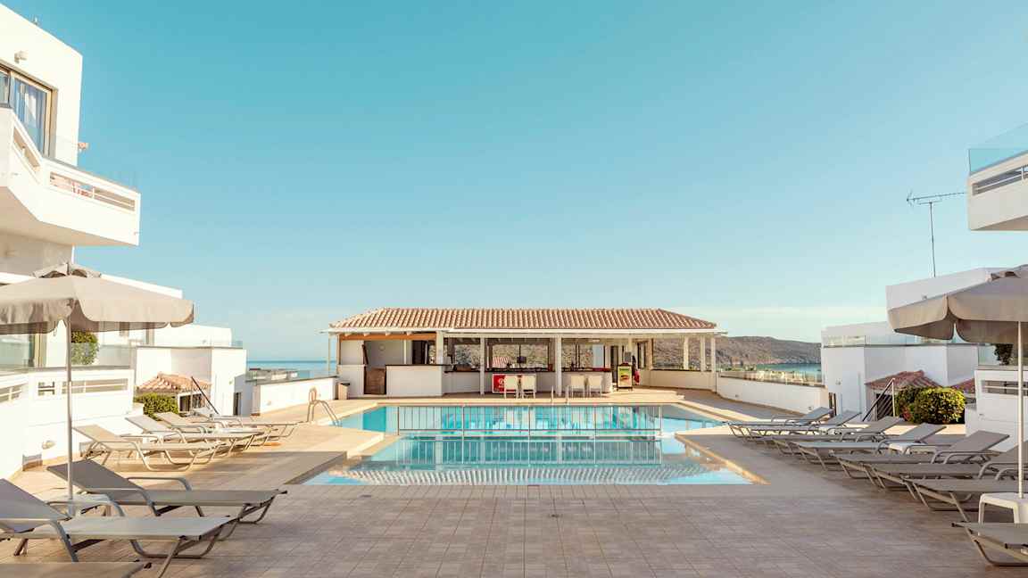 Hotelpoolområde med liggestole, parasoller og blå himmel. (AI-genereret tekst)