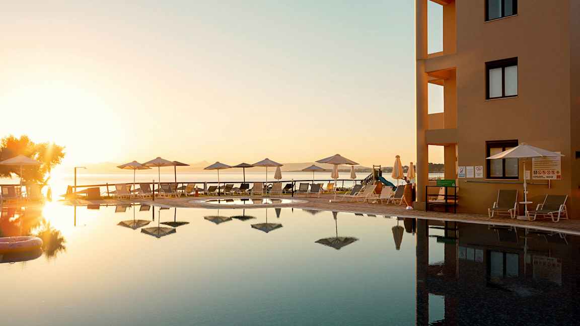 Et poolområde ved en bygning med udsigt over havet under en solnedgang. (AI-genereret tekst)