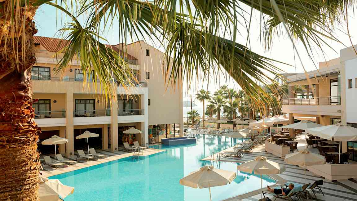 Hotel med udendørs pool, liggestole og parasoller. (AI-genereret tekst)