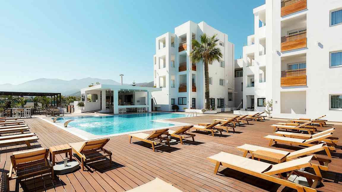 Udendørs poolområde med liggestole, moderne bygning og blå himmel. (AI-genereret tekst)