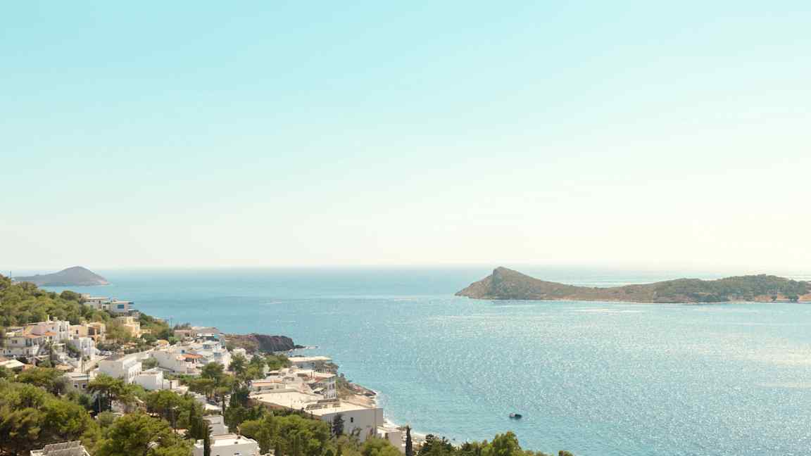 Udsigt over kystlinje med hvide bygninger og grønne træer, havet og en ø i baggrunden. (AI-genereret tekst)