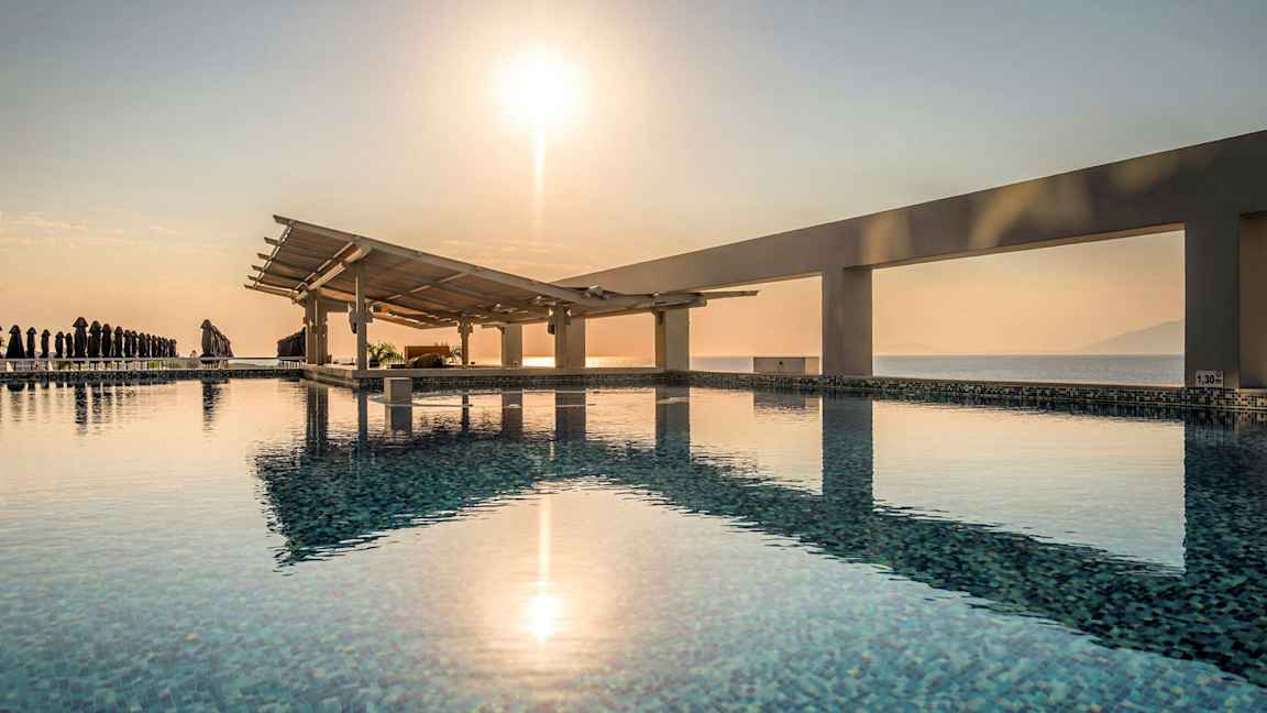 En pool med udsigt over havet og en solopgang. (AI-genereret tekst)