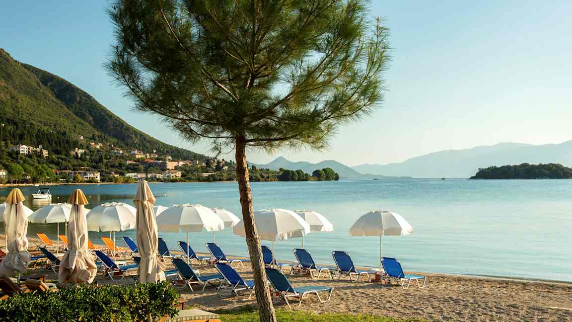 En strand med liggestole, parasoller og udsigt over havet med bjerge i baggrunden. (AI-genereret tekst)