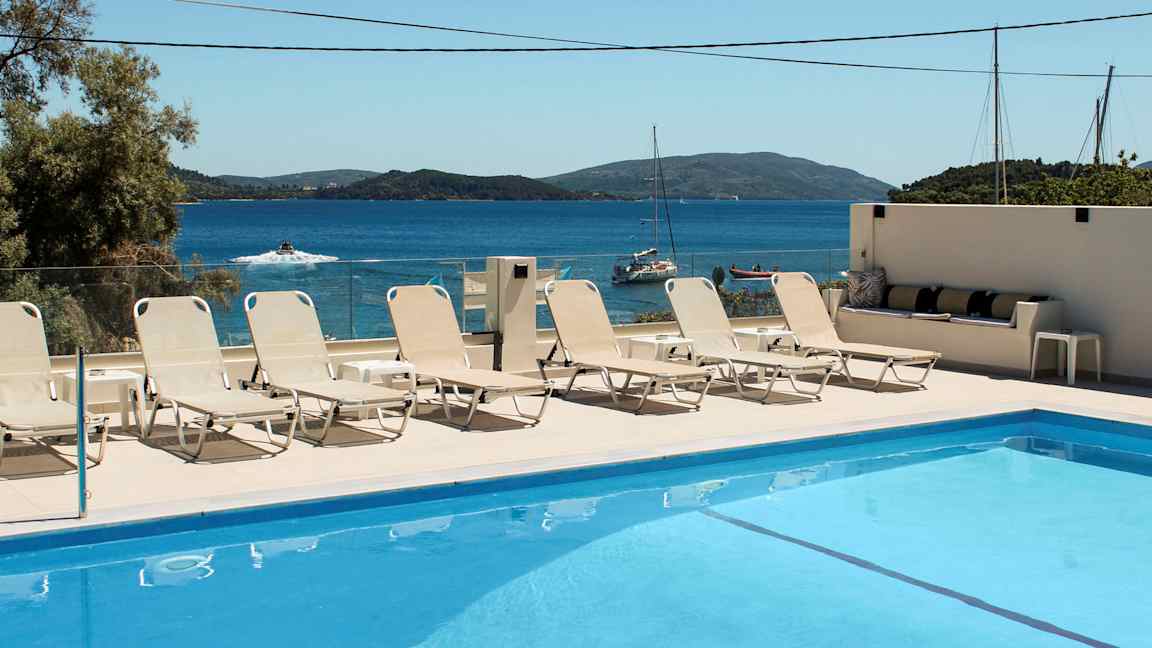 Swimmingpool med liggestole og havudsigt i baggrunden. (AI-genereret tekst)