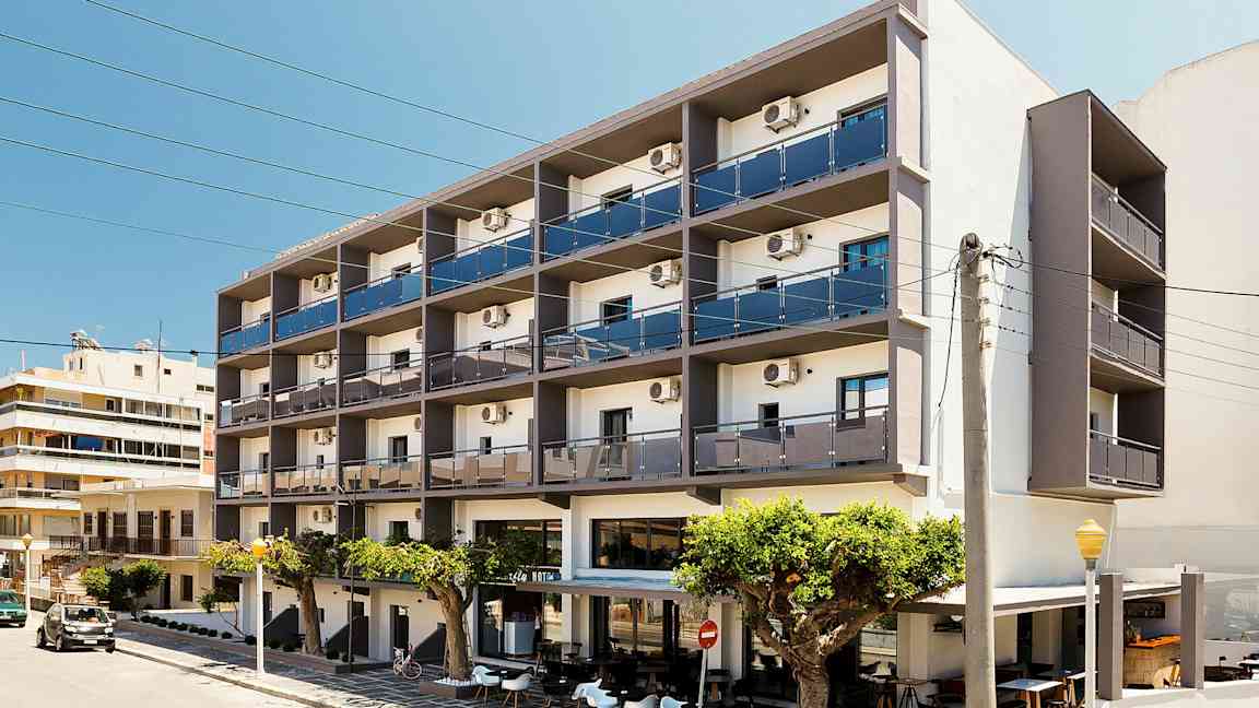 Et fleretagers hotel med altaner og udendørs servering foran, beliggende ved en gade. (AI-genereret tekst)