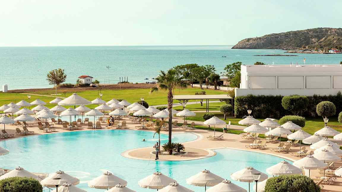 En pool med liggestole og parasoller, med udsigt til havet og frodige omgivelser. (AI-genereret tekst)