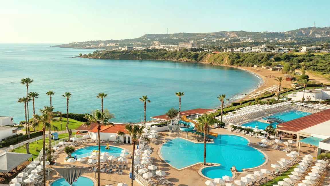 Udsigt over hotelområde med pools, liggestole og havudsigt. (AI-genereret tekst)