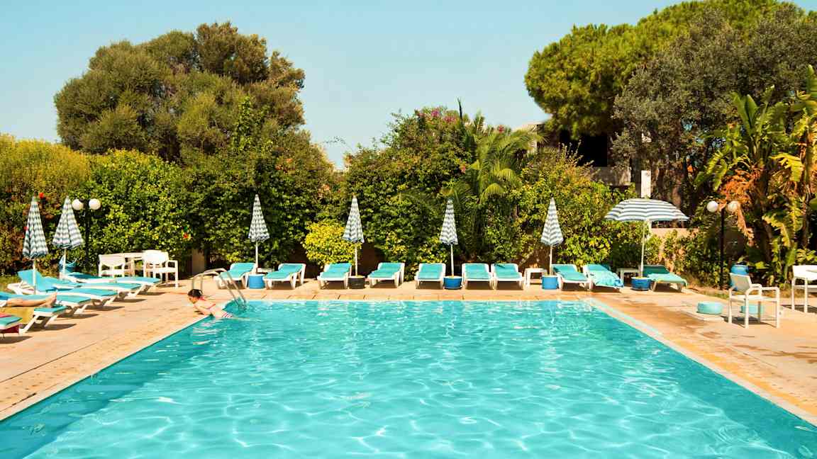 Udendørs pool omgivet af liggestole, parasoller og grønne planter. (AI-genereret tekst)