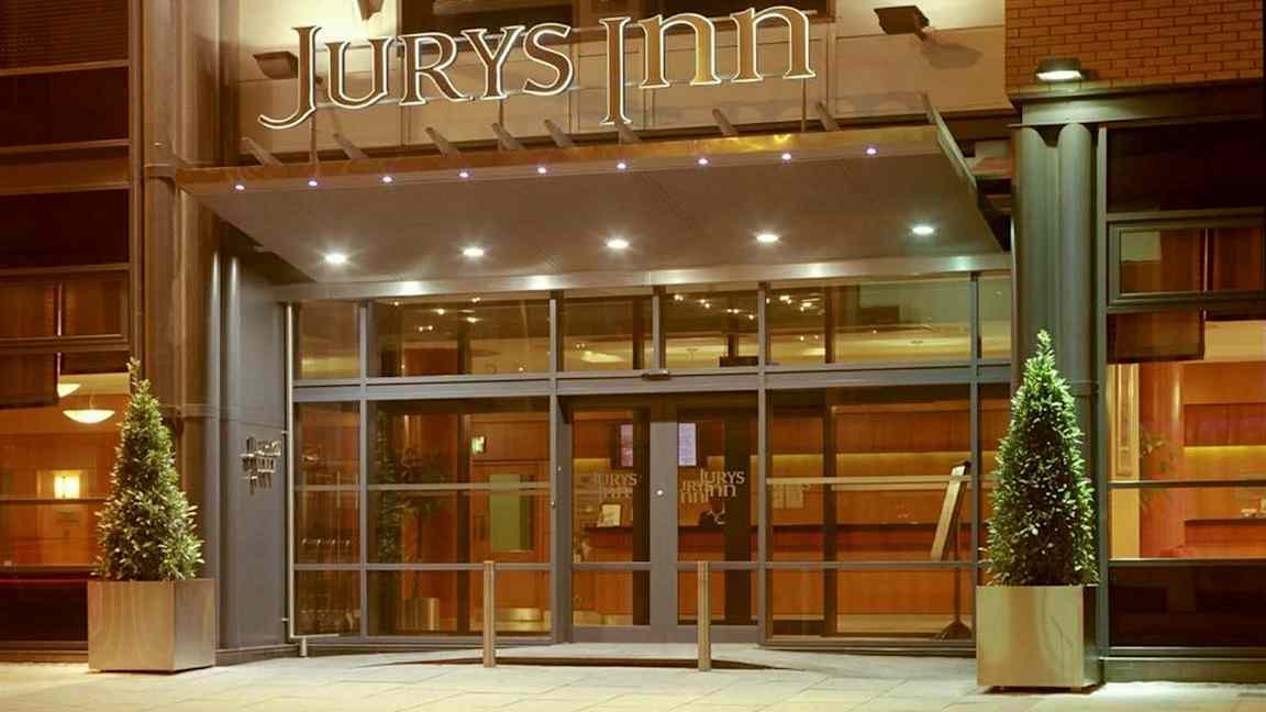 Hotelindgang med glasdøre og skiltet 'Jurys Inn' ovenfor. (AI-genereret tekst)