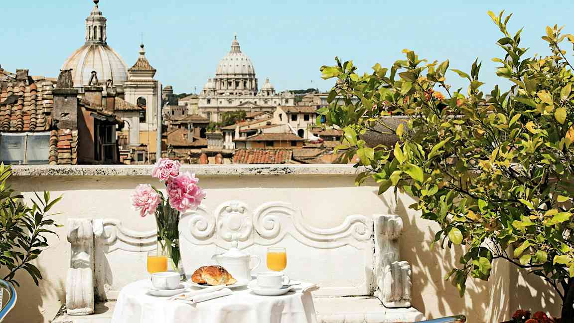 En terrasse med et bord dækket til morgenmad og udsigt over byens tage og en katedral. (AI-genereret tekst)