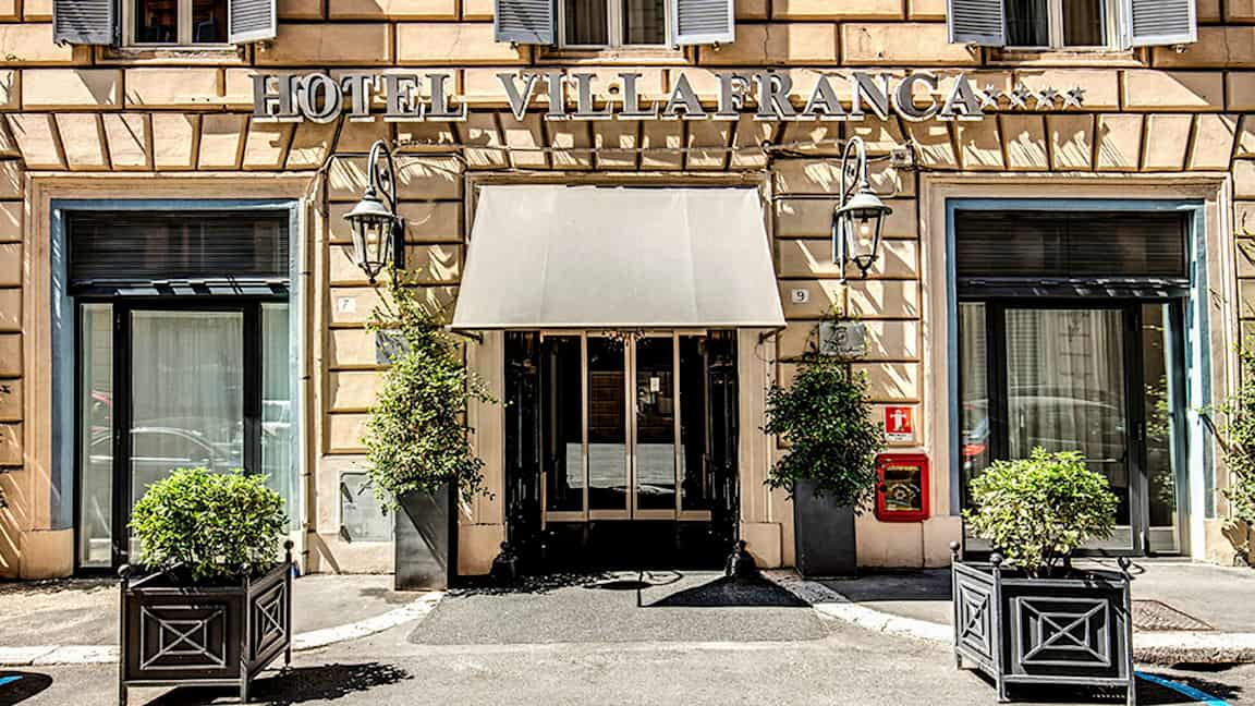 Hotelindgang med skilt, vinduer og planter i potter. (AI-genereret tekst)