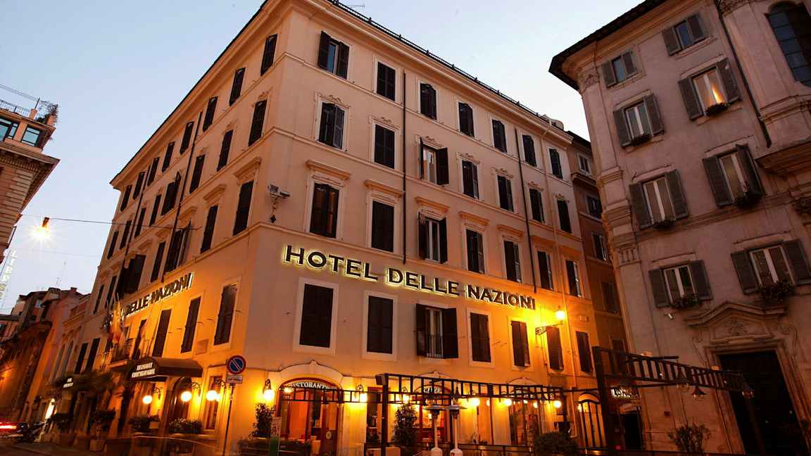 Billede af en bygning med skilt, der siger Hotel Delle Nazioni, oplyst med aftenbelysning. (AI-genereret tekst)
