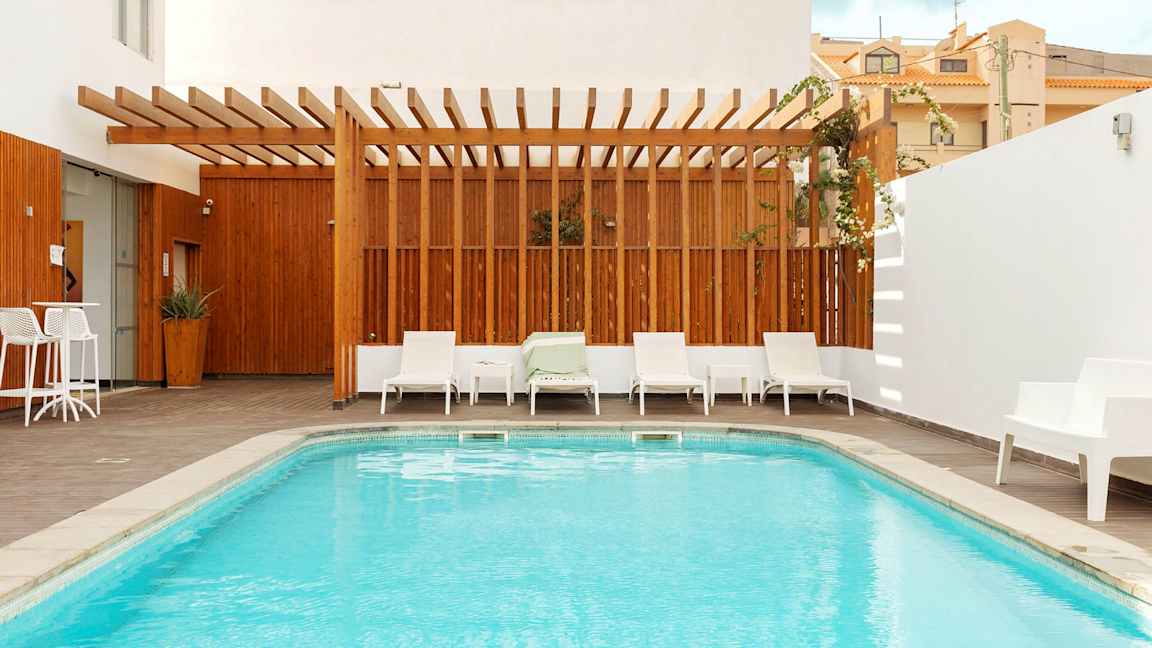 En lille pool med omgivende liggestole og træterrasse, en træramme skaber en afskærmet atmosfære. (AI-genereret tekst)