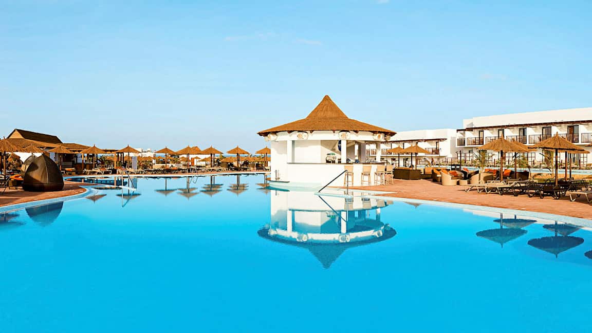 En stor pool med parasoller og siddepladser ved et hotelområde. (AI-genereret tekst)