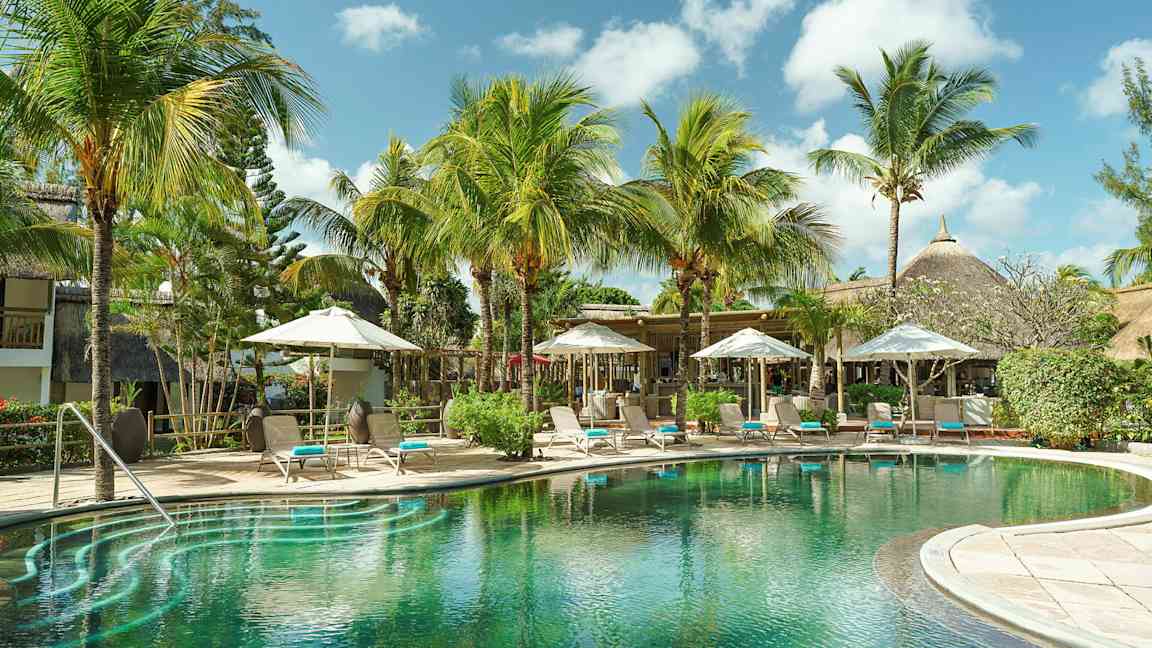 En eksotisk pool omgivet af palmer og liggestole under parasoller. (AI-genereret tekst)