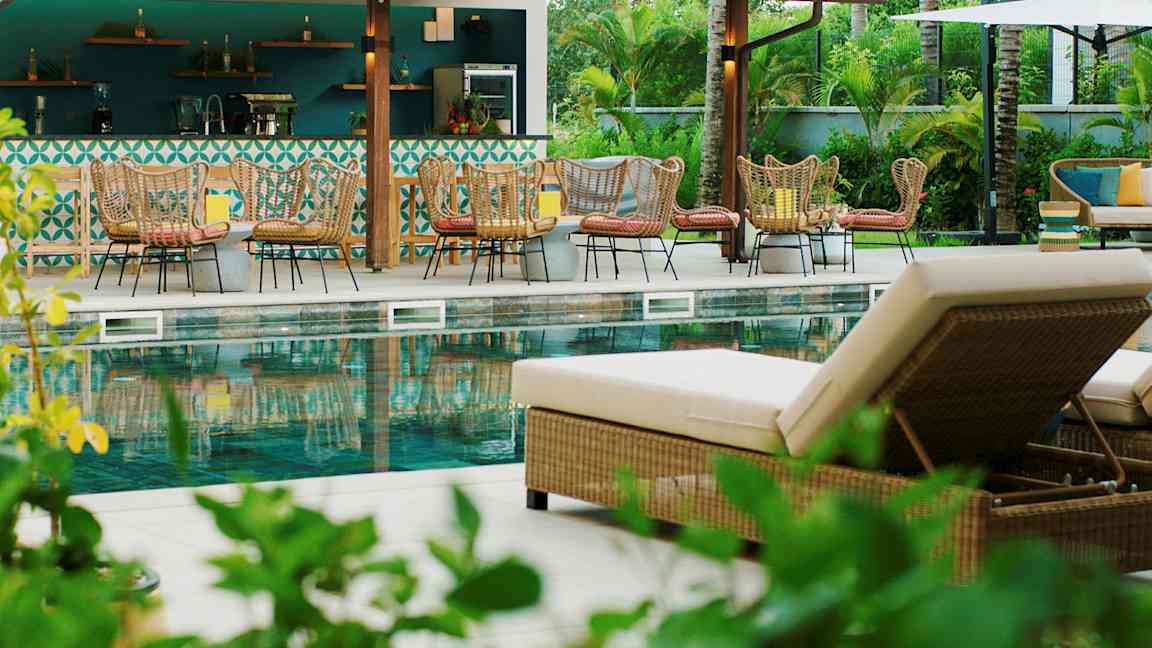 En udendørs swimmingpool med liggestole og siddegrupper ved en bar. (AI-genereret tekst)