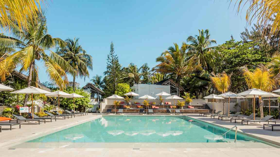 En pool omgivet af liggestole og parasoller med palmer i baggrunden. (AI-genereret tekst)