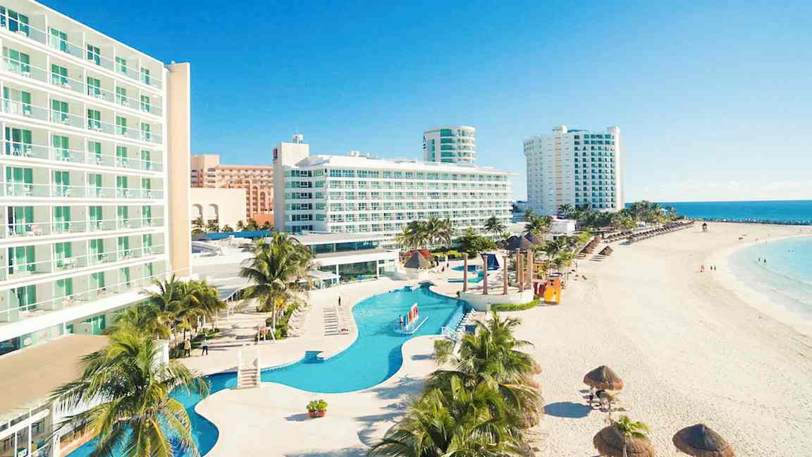 Billede af hotel ved stranden med pool og palmer. (AI-genereret tekst)
