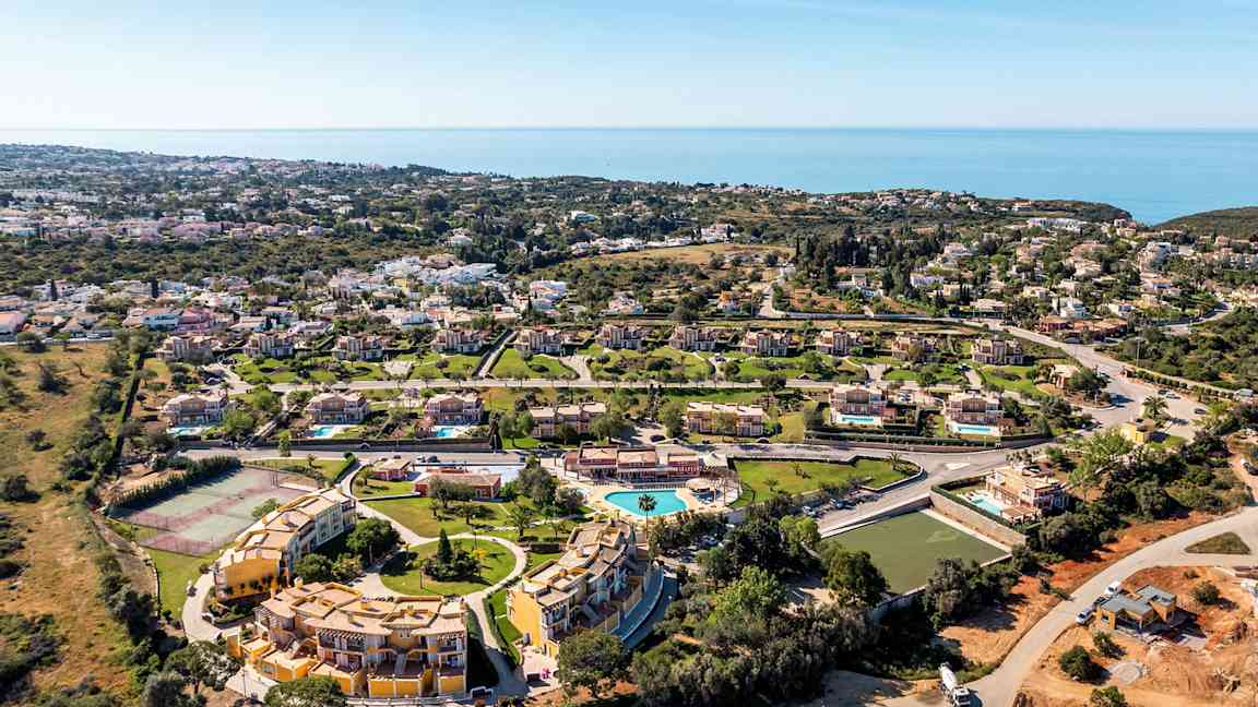 Luftfoto af et ferieområde med villaer, swimmingpool og havudsigt. (AI-genereret tekst)