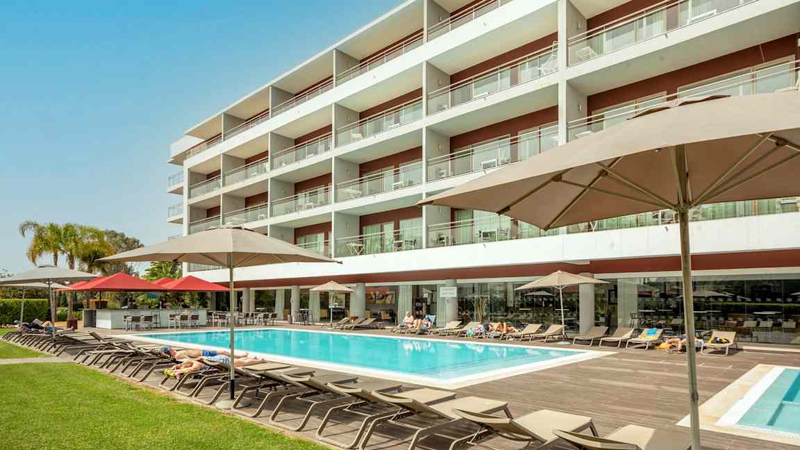 Hotelbygning med pool og liggestole. (AI-genereret tekst)