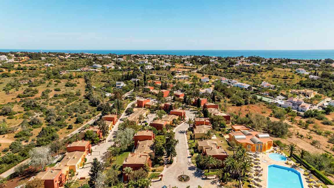 Luftfoto af et feriekompleks med villaer og pools omgivet af grønne områder. (AI-genereret tekst)